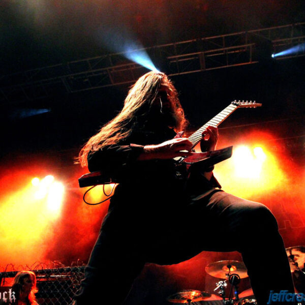 A man with long hair playing a guitar on stage.