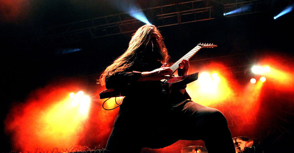 A man with long hair playing a guitar on stage.