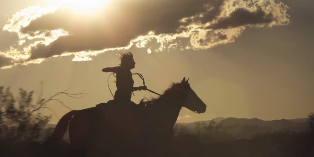 A silhouette of a man riding a horse in the desert.