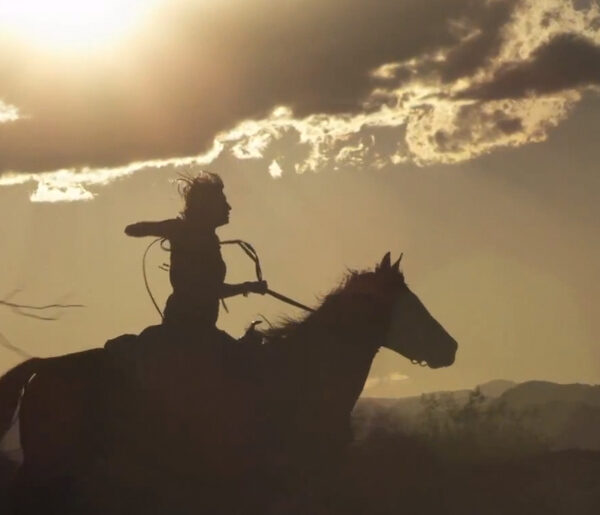 A silhouette of a man riding a horse in the desert.