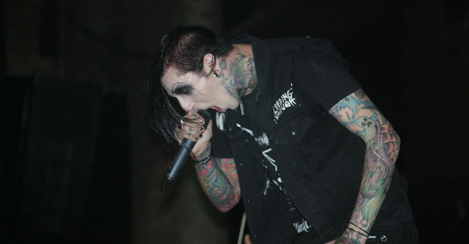 A man with tattoos singing into a microphone.