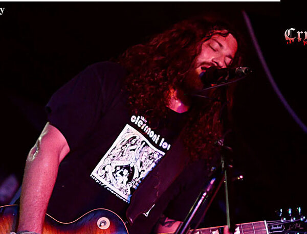 A man with long hair playing a guitar in front of a microphone.