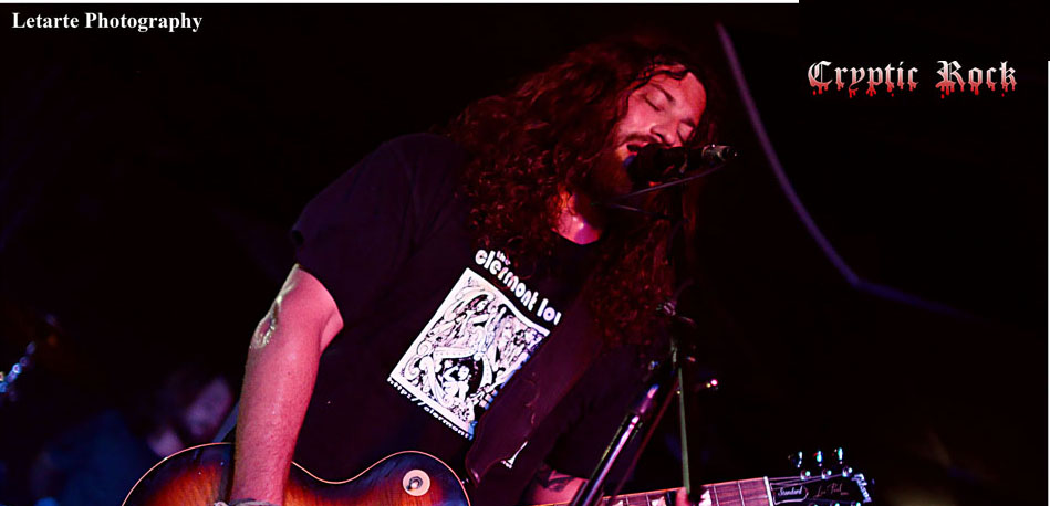 A man with long hair playing a guitar in front of a microphone.