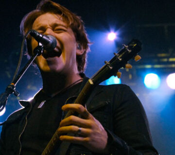 A man singing into a microphone while holding a guitar.