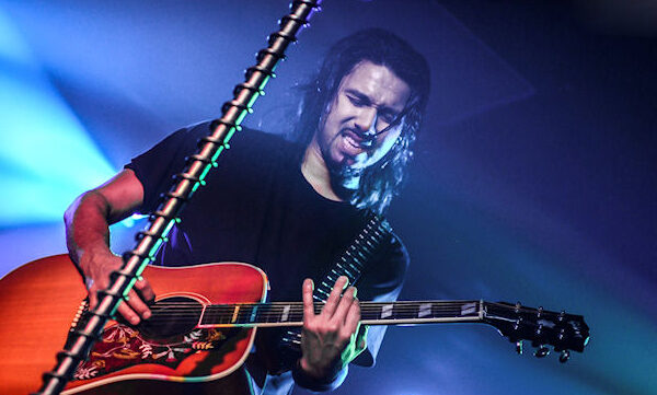 A man with long hair playing an acoustic guitar.