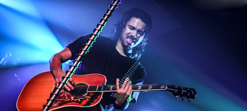 A man with long hair playing an acoustic guitar.